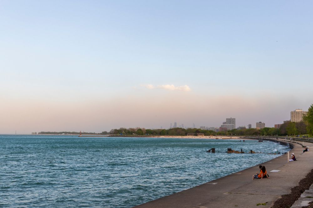 A haboob, or dust storm, appears on the horizon as a brownish layer below an otherwise clear blue sky. Slightly choppy Lake Michigan waters, still quite blue, appear in the foreground. The Chicago skyline is becoming obscured.