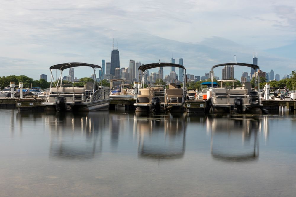 Three matching boats with canopies on top of them sit quietly in Diversey Harbor in Chicago on a sleepy Saturday morning. With a second of exposure time, the water in front of the boats looks more like a mirror than usual but otherwise it's hard to tell it's a long exposure. Behind the rows and rows of boats and beneath an overcast sky, the Chicago skyline