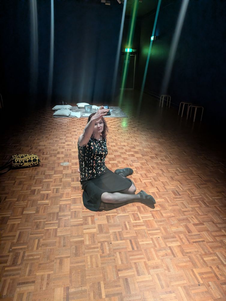 Frames sitting on the floor of an art gallery taking a selfie. In the background there is an art on the floor. 