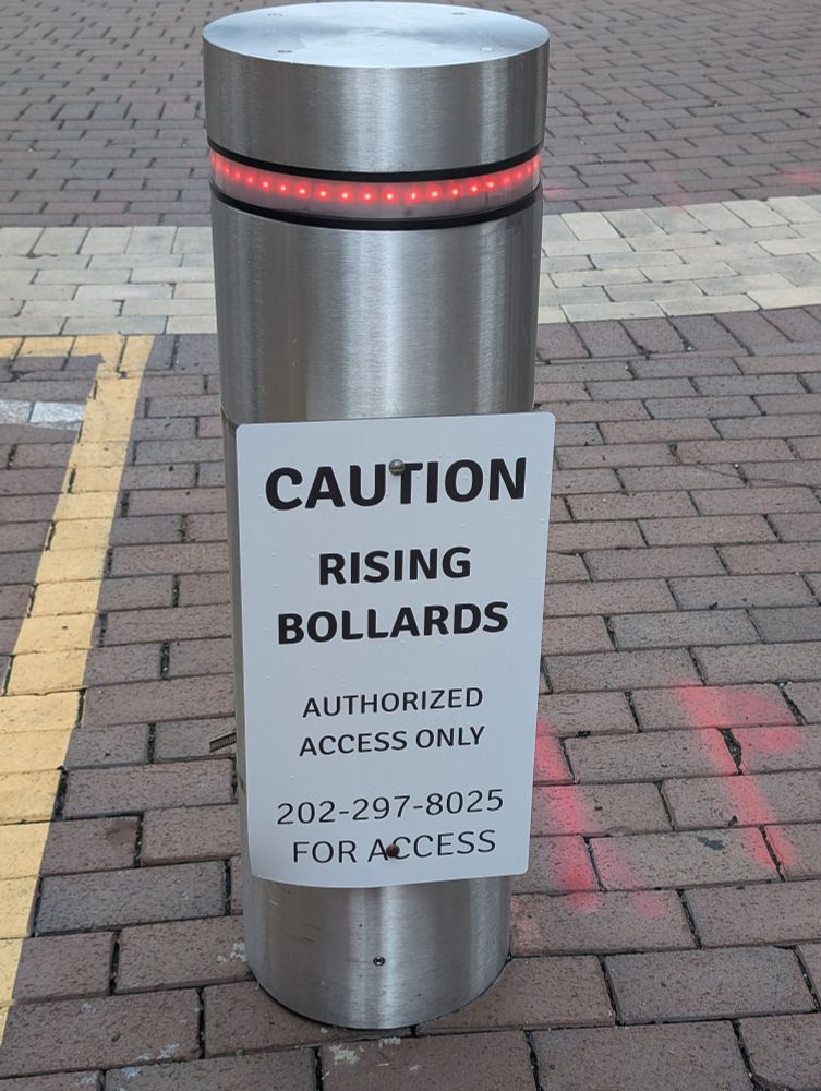 Silver bollard with sign: caution rising bollards authorized access only