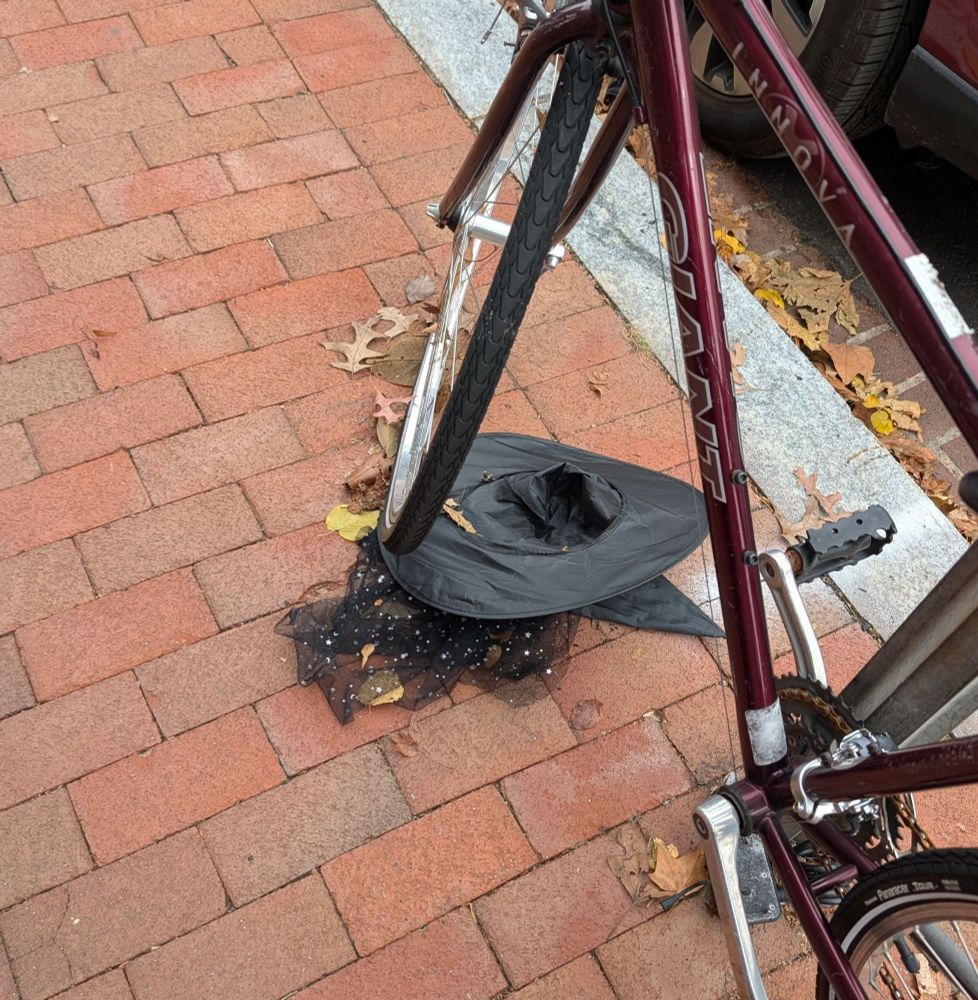 Bike on the sidewalk with a witch's hat trapped under the front wheel