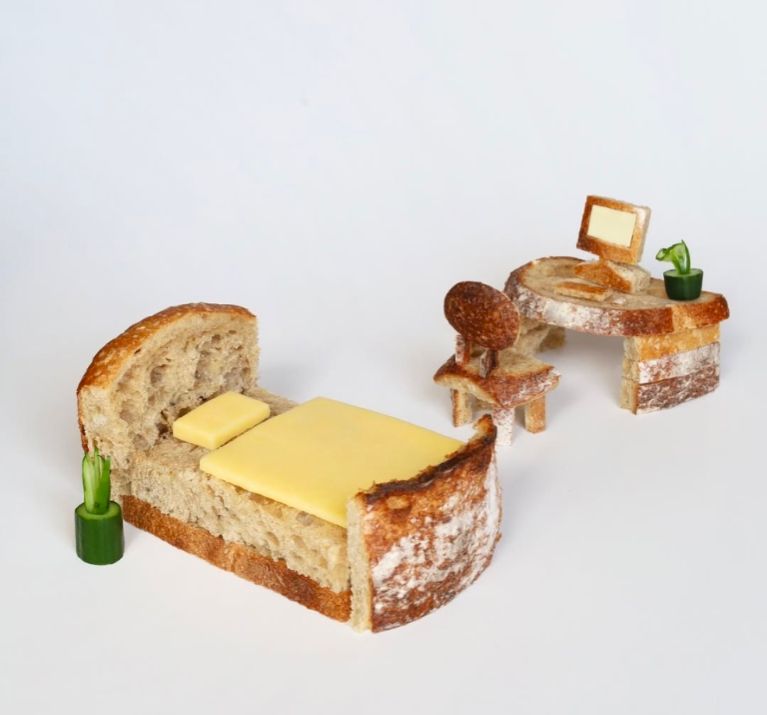 Tiny bedroom scene made entirely of bread and cheese with some cucumbers
