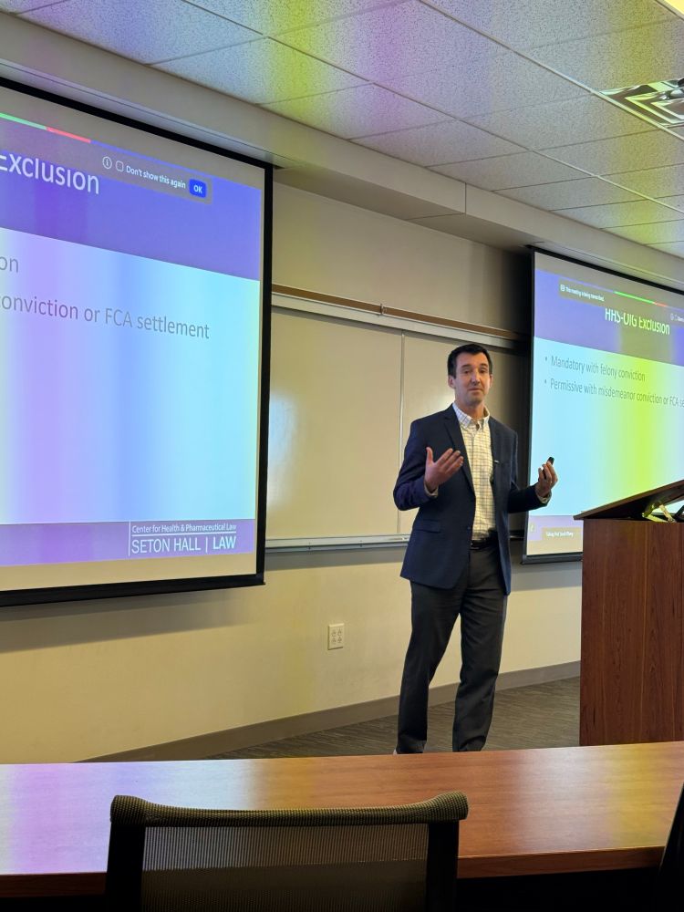 Prof Elberg standing at lecturn speaking in front of projected PowerPoint slides. No slide content shown in picture. 
