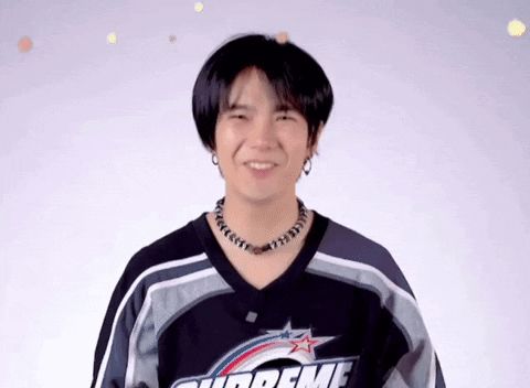 a young man wearing a supreme jersey and a necklace is smiling and looking at the camera .