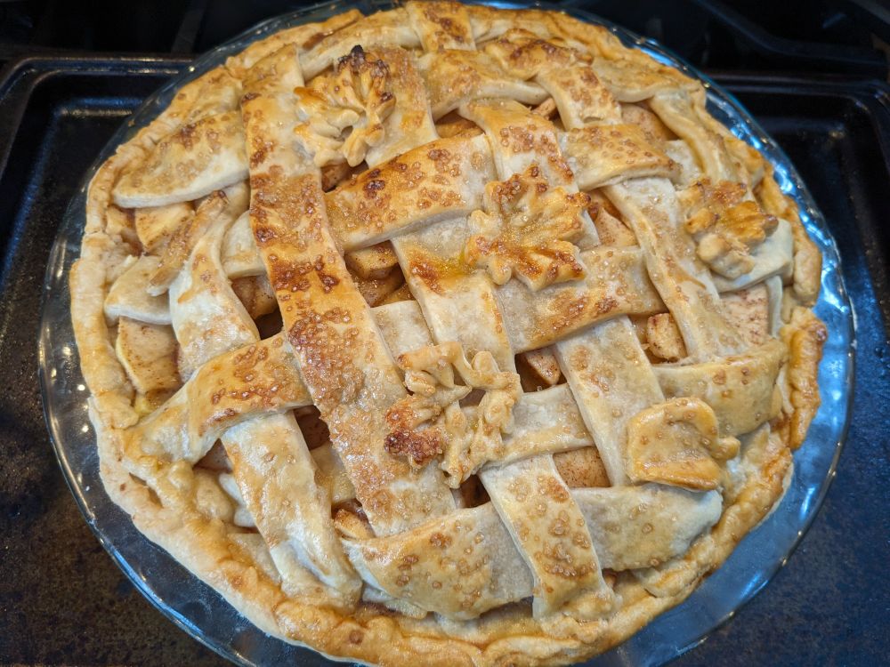 an apple pie, fresh out of the oven. it has a mostly correct lattice crust with maple leaf and apple shaped decorations made out of extra pie crust