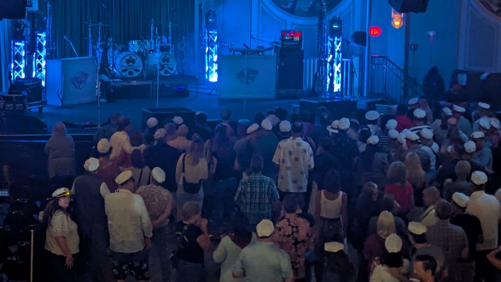 A crowd around a stage, with many wearing white captain's hats