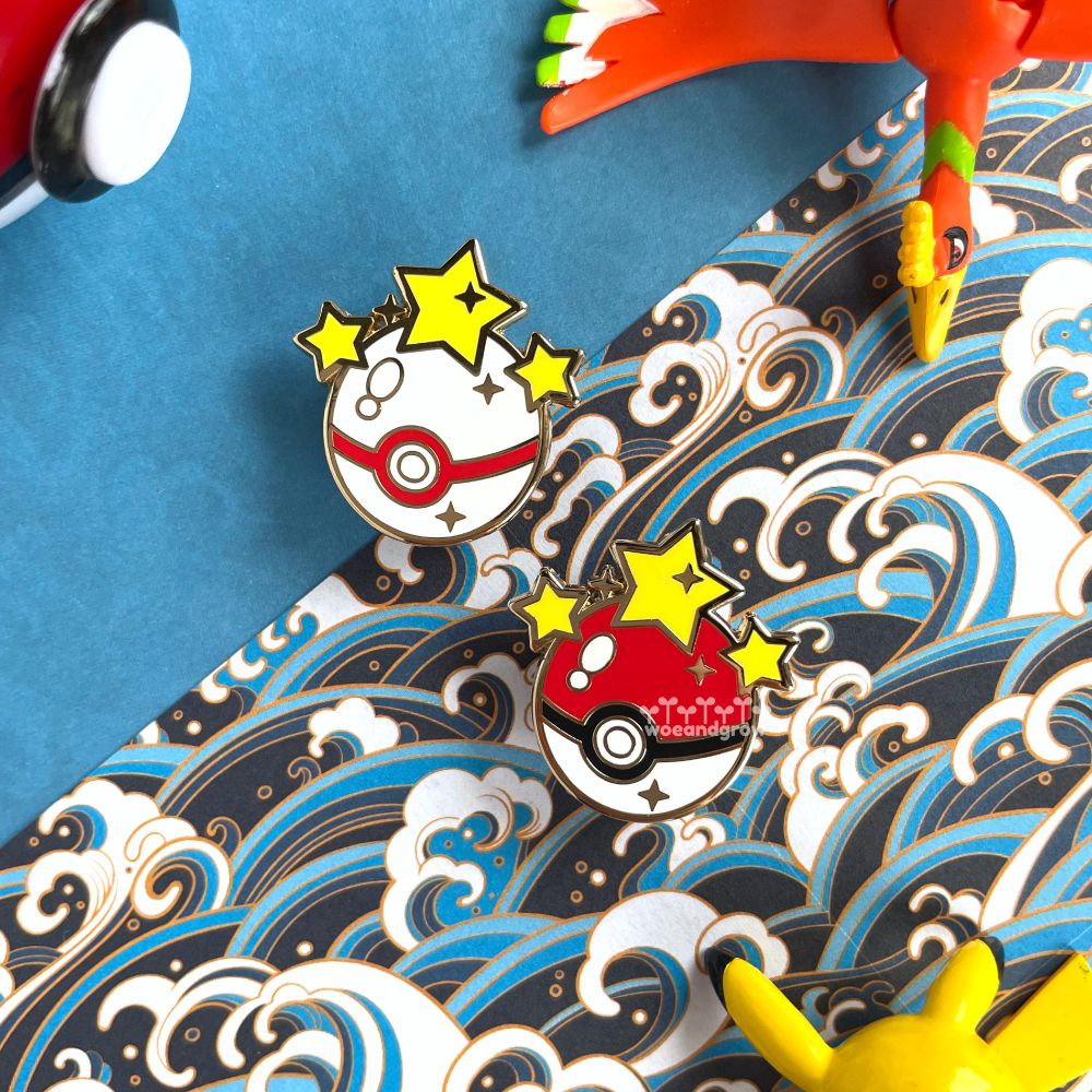 Closeup photo of my Gotcha! Poke Ball and Premier Ball enamel pins surrounded by various Pokemon props