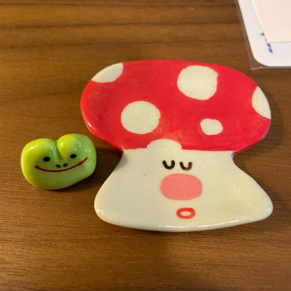 Photo of two ceramic pieces, one of a small smiling frog head and the other a small mushroom dish with a calm expression