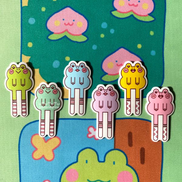 Closeup photo of my Frogs with Socks stickers lined up. Each frog is a different color with varying expressions and sock types/patterns.