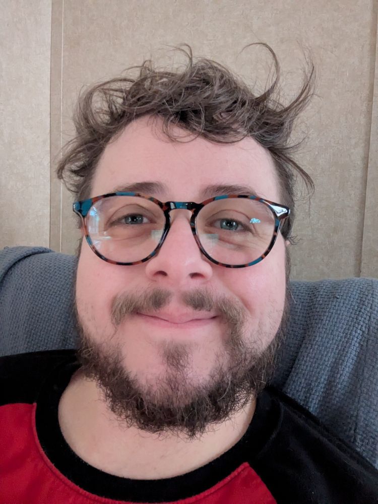 Person with bedhead wearing glasses smiling 