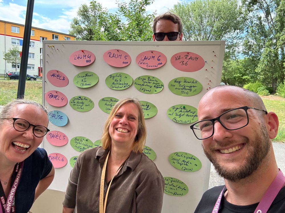 Sessionplancrew - drei Personen lachen vor einer Wand mit Themen, eine Person schaut hinter der Wand hervor 