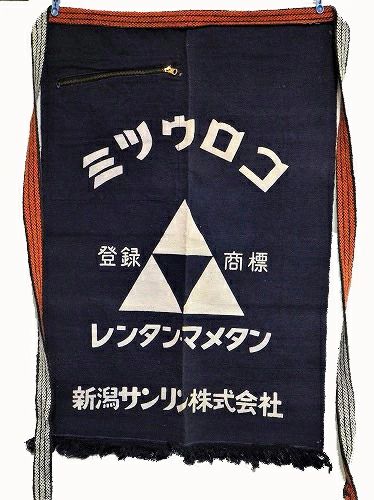 The image shows a traditional Japanese work apron made of dark blue fabric. The apron has two long, thick orange straps with a white black pattern hanging from each side, allowing it to be tied around the waist. Near the top left, there is a small zippered pocket.

Printed on the center front in white, there is a design featuring three white triangles arranged in such a way that they form a larger triangle with a smaller, inverted triangle of dark blue in the center. Japanese text is printed in several places around the triangles, both above and below them.

This is likely the logo and branding for a company. The overall appearance is utilitarian, traditional, and practical.