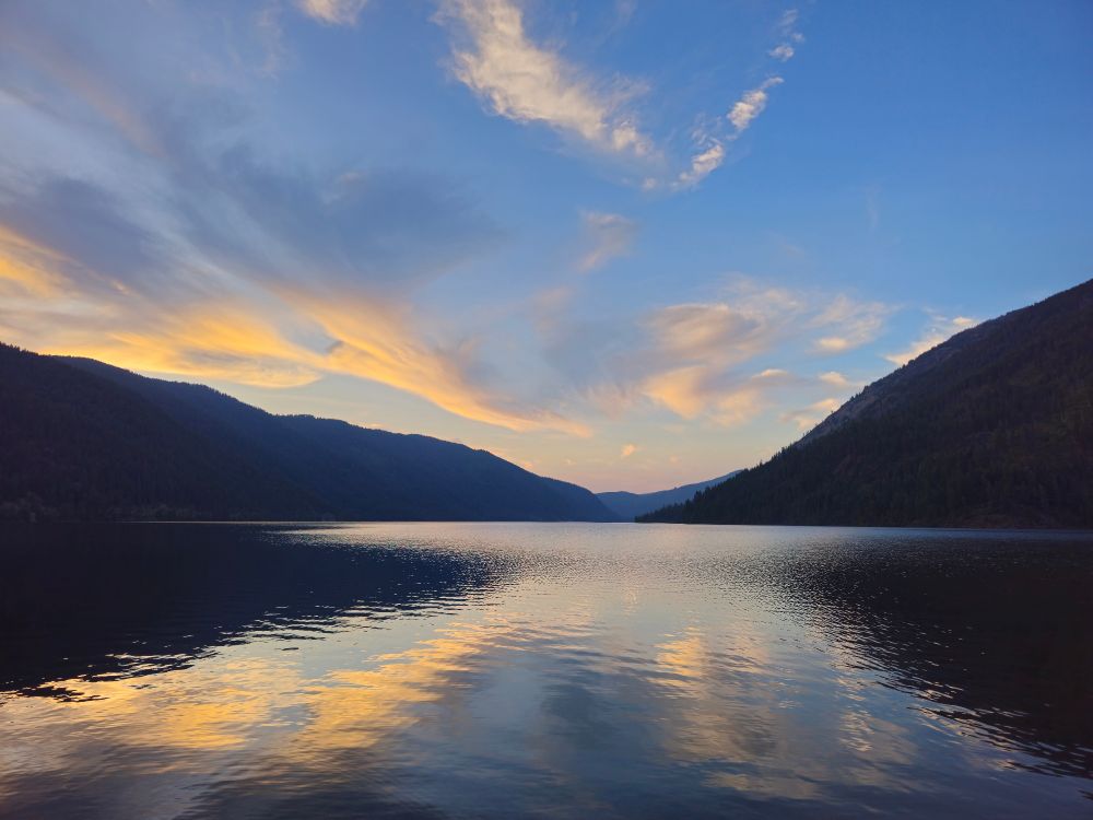 The setting sun casts a warm glow on clouds above a calm lake in Washington 