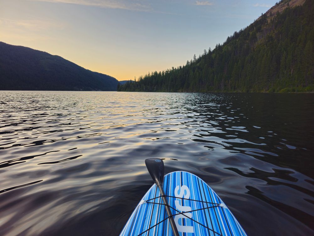 A paddle board sits on a calm lake with green hills coming down to the waterline in Washington 