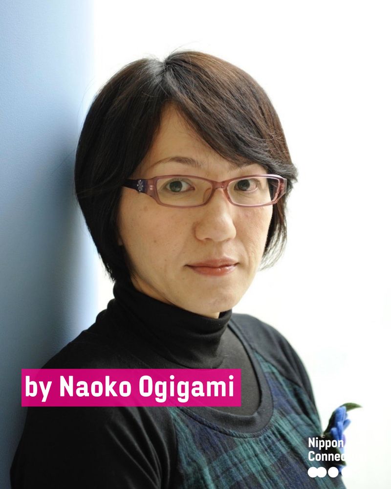 Porträt der Regisseurin Naoko Ogigami. Sie lehnt an einer Wand, trägt eine Brille und schaut ruhig in die Kamera.