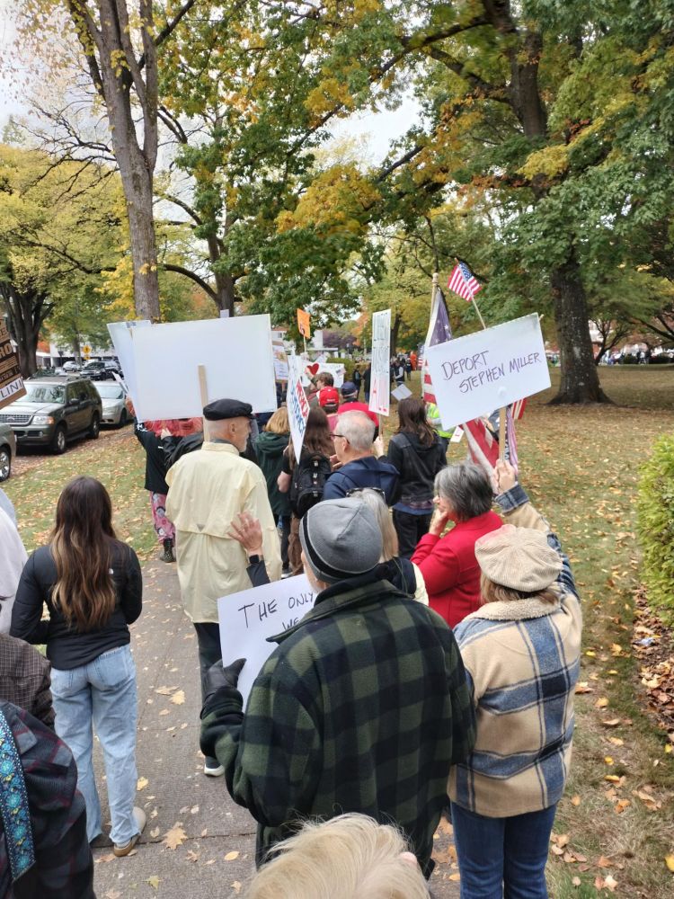A long line of protestors all the way down the sidewalk and around the corner at a park 