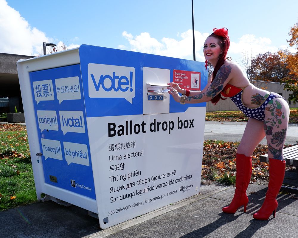Burlesque performer Scarlett O'Hairdye dressed in a sexy Wonder Woman swimsuit and knee high red high heeled boots poses inserting a ballot into a King County ballot drop box.