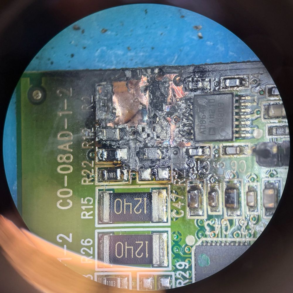 A charred circuit board. Several components are damaged and you can see bare copper and fiberglass.