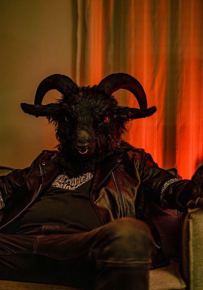 Wearing my fursuit head of Pazu, the satanic goat, leather jacket and other metal fashion clothes, sitting in an armchair with red lighting for a more sinister look.