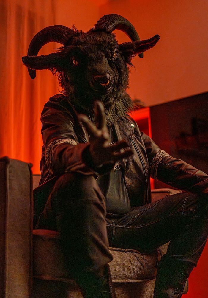 Wearing my fursuit head of Pazu, the satanic goat, leather jacket and other metal fashion clothes, sitting in an armchair with red lighting for a more sinister look.