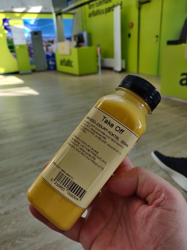 A bottle of mango and yoghurt smoothie you can get at the airport, with boarding gate in the background.