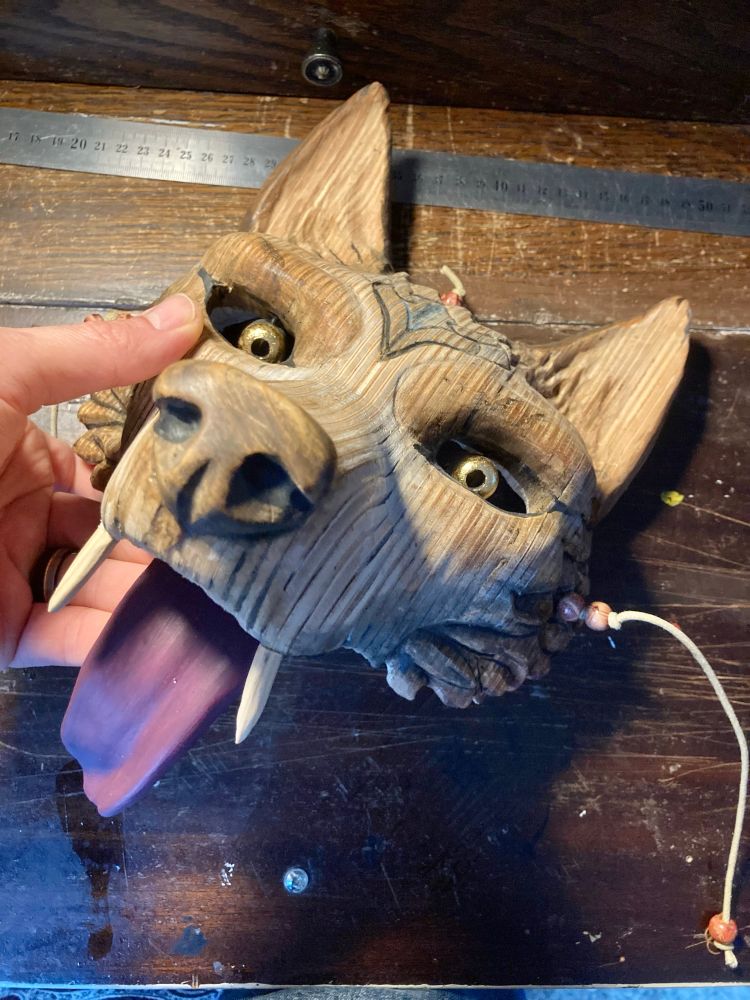 Full shot of artwork being held on a work desk, beech wood mask depicting a wolf form