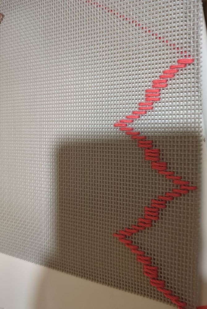 Material gris, maleable, de huequitos rectangulares. Tiene una pequeña zona bordada con un color coral maravilloso