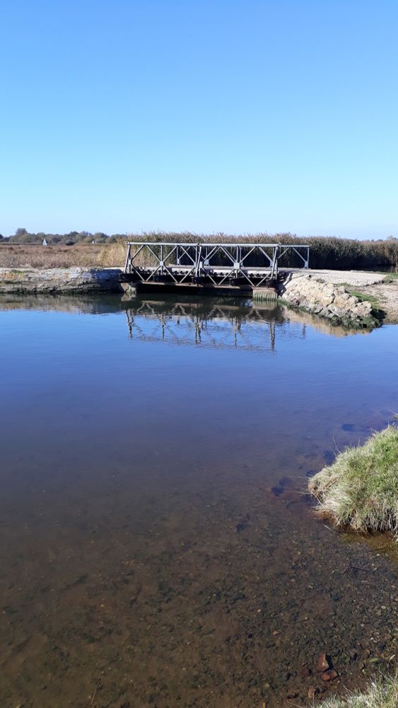 A short Bailey bridge on a sunny day. The bridge & the blue sky are reflected in the water.