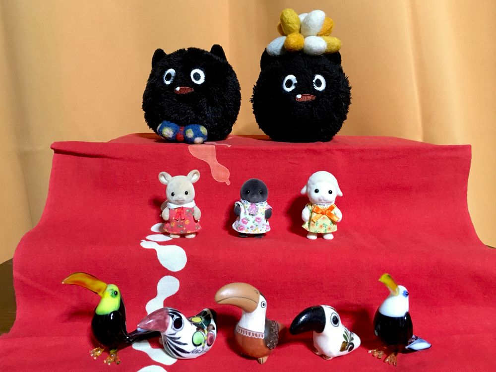 階段状になったところに赤い手拭いを敷き、上段にふたつのカーバンクルのぬいぐるみ、中段に三つのシルバニアファミリーの赤ちゃん、下段に五つの小さなオオハシの置物を飾って、三段飾りのお雛様を模している