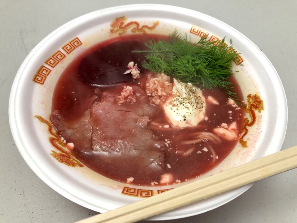 ビーツの色が出たスープの中に麺が入り、トッピングに牛叉焼、ディル、サワークリーム、ニンニクの入った真っ赤な色のボルシチラーメン