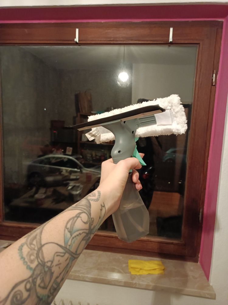 ein kombi-fensterputzgerät wird in die kamera gehalten. im hintergrund ist ein großes fenster zu sehen. durch das fenster sieht man kein tageslicht, es ist nachts