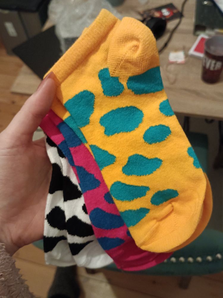 es werden drei paar bunt gefleckte sneaker-socken in die kamera gehalten. die socken haben folgende Farbkombinationen: schwarz/weiß, magenta/blau, gelb/türkis 