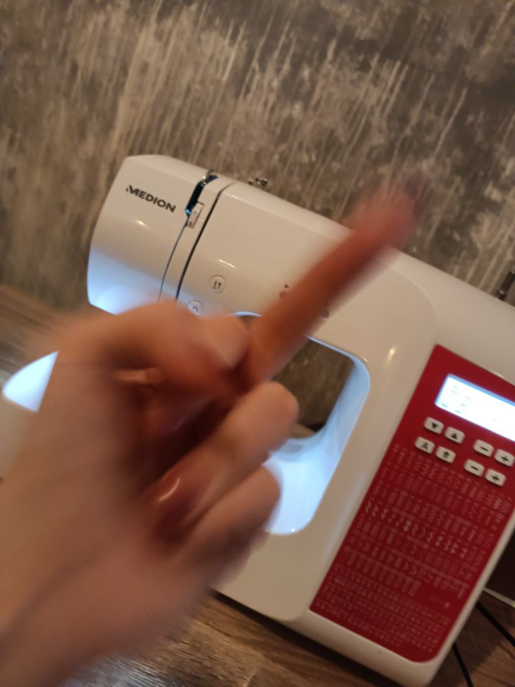 eine hand streckt einer Nähmaschine den mittelfinger entgegen. 