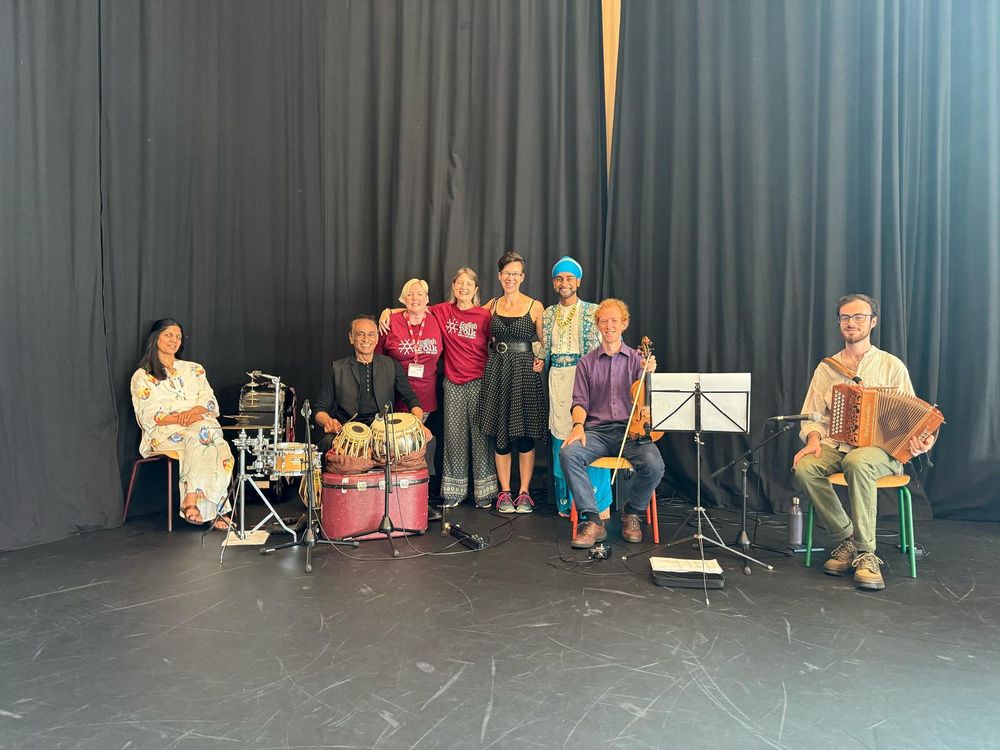 A group of musicians, callers and staff from English Folk Dance and Song Society stand in front of a curtain with their instruments 