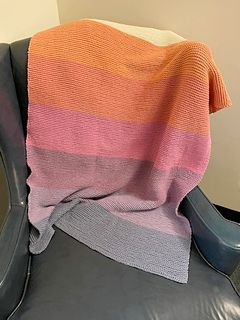 A rainbow-striped baby blanket hangs over the back of a blue leather wing chair.