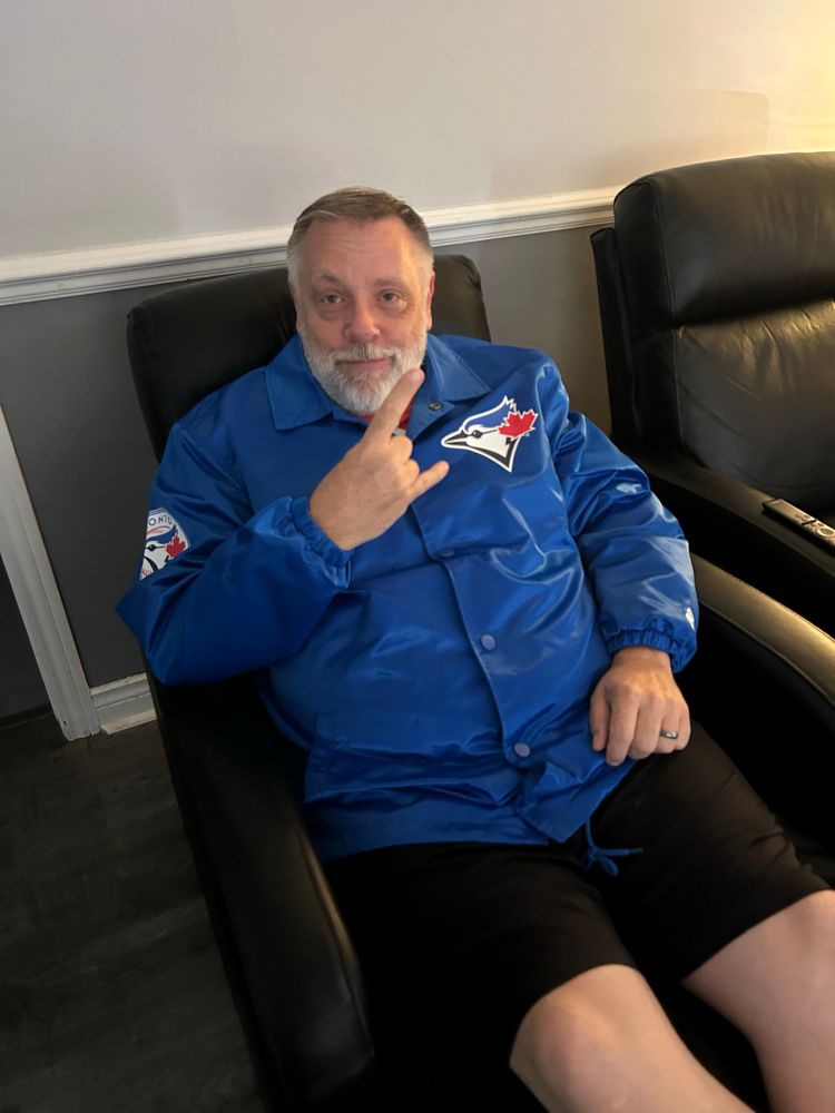 A man sitting in a recliner chair wearing a Toronto Blue Jays jacket . 