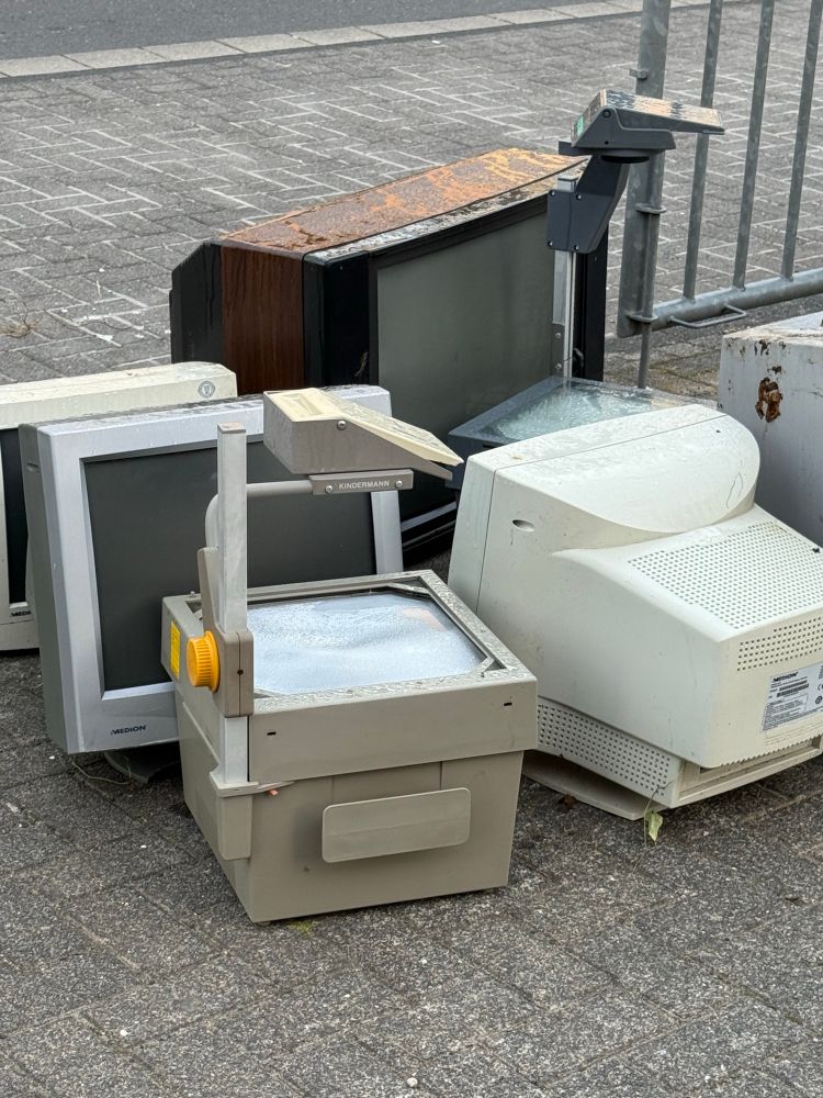 diverse alte Röhrenmonitore und Overheadprojektoren am Straßenrand.