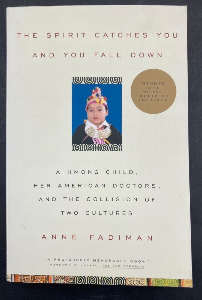 cream book cover against a black background. The title of the book is "The Spirit Catches You and You Fall Down", the subtitle is "A Hmong Child, Her American Doctors, and The Collision of Two Cultures", and  the author is Anne Fadiman. The cover has a sticker, "Winner of the National Book Critics Circle Award"