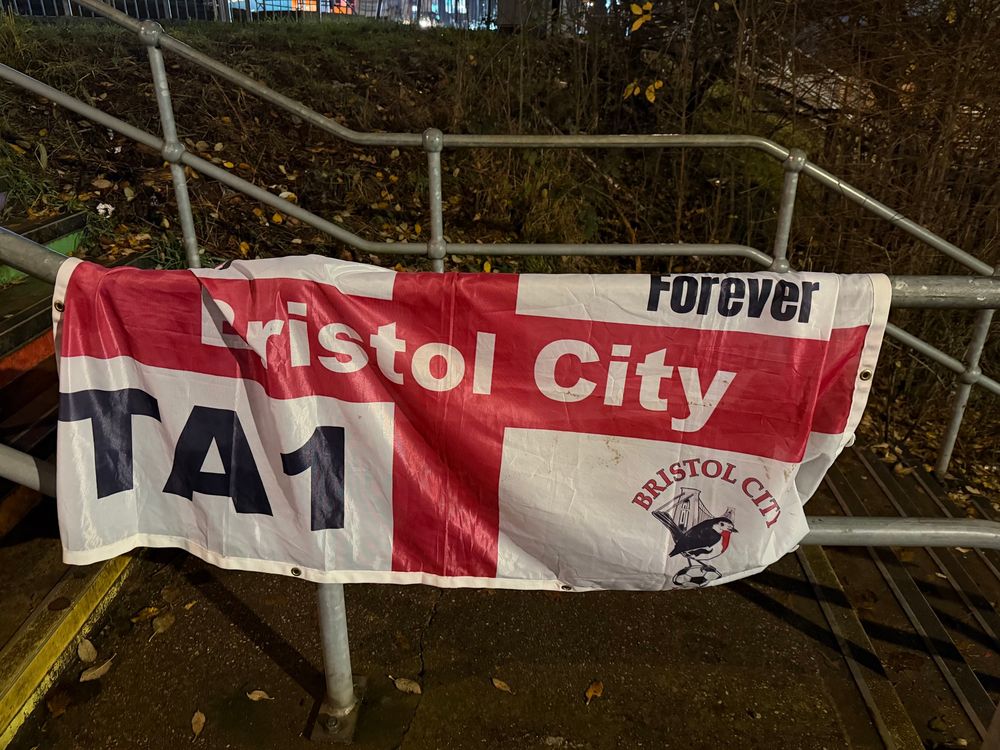 An abandoned St George’s Cross flag, with the text ‘Bristol City’ against the Red Cross, ‘TA1’ in the bottom left corner, an older version of the club crest in the bottom right, and the text ‘Forever’ in the top right