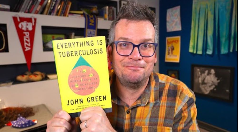 John Green holding his book "Everything Is Tuberculosis" (2025), a New York Times number one bestseller in nonfiction.