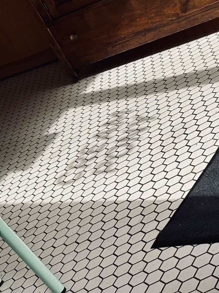 A shadow is cast on a hexagonal tiled floor, spelling out “cream pony”, partially obscured by a wooden cabinet. A corner of a black mat is visible in the image.
