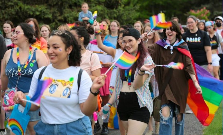 People with rainbow flags and accessories walk through Porter Park. 