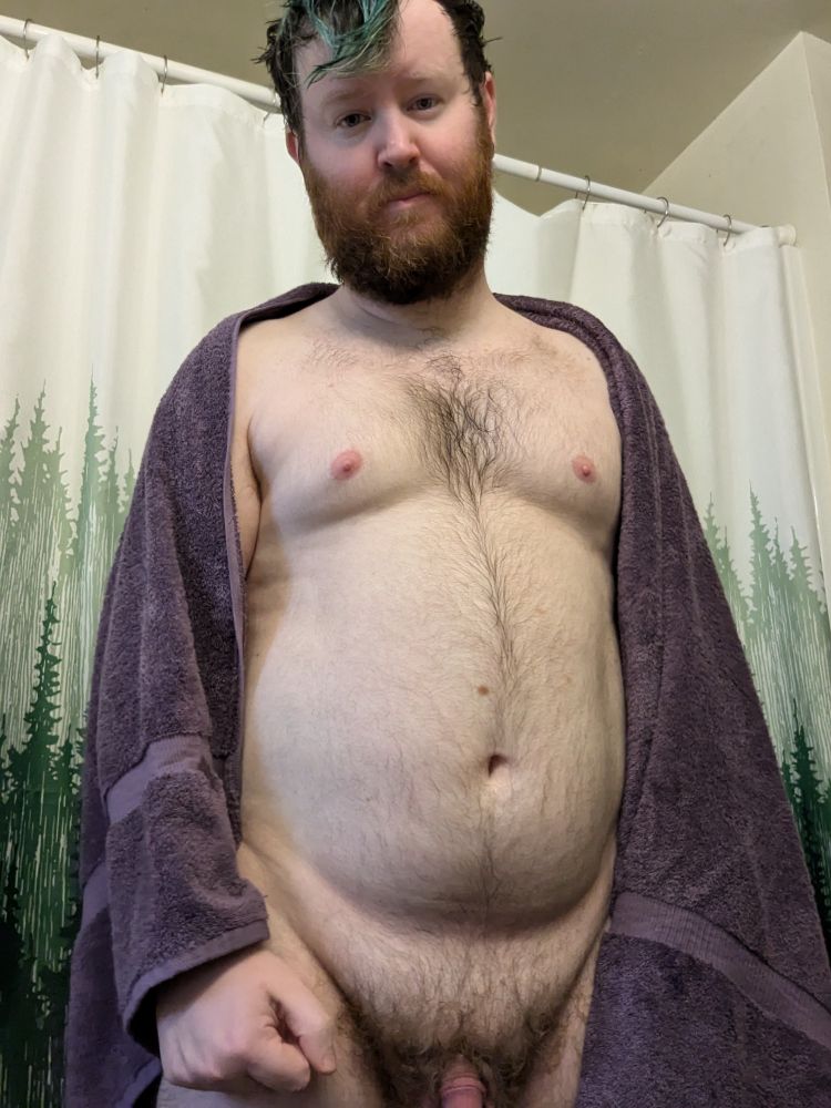 A person standing in front of a shower curtain with a towel drapes over their shoulder.