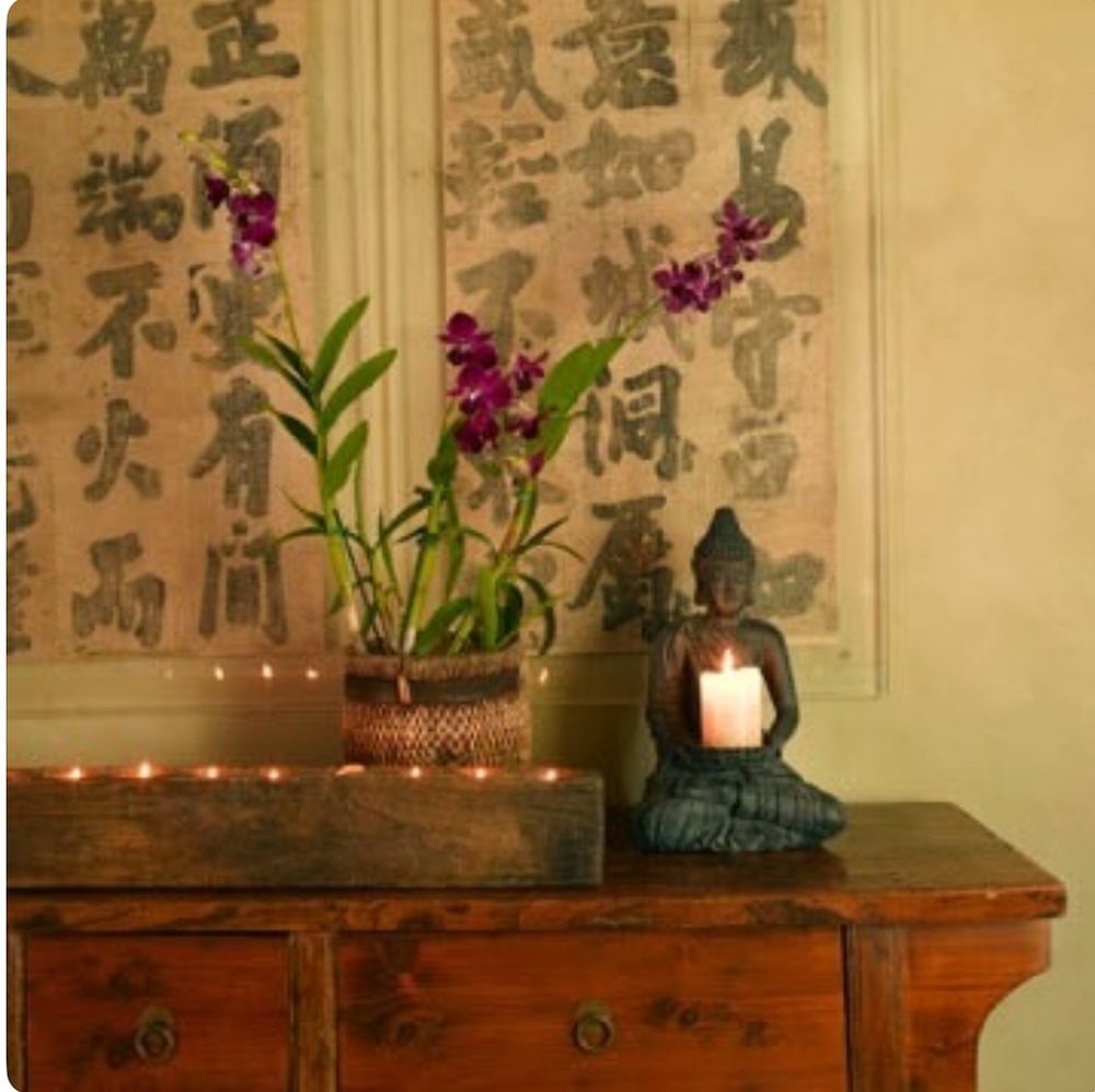 Wood tabletop with candles, Buddha image holding a candle, blooming orchid, and framed Chinese calligraphy. 