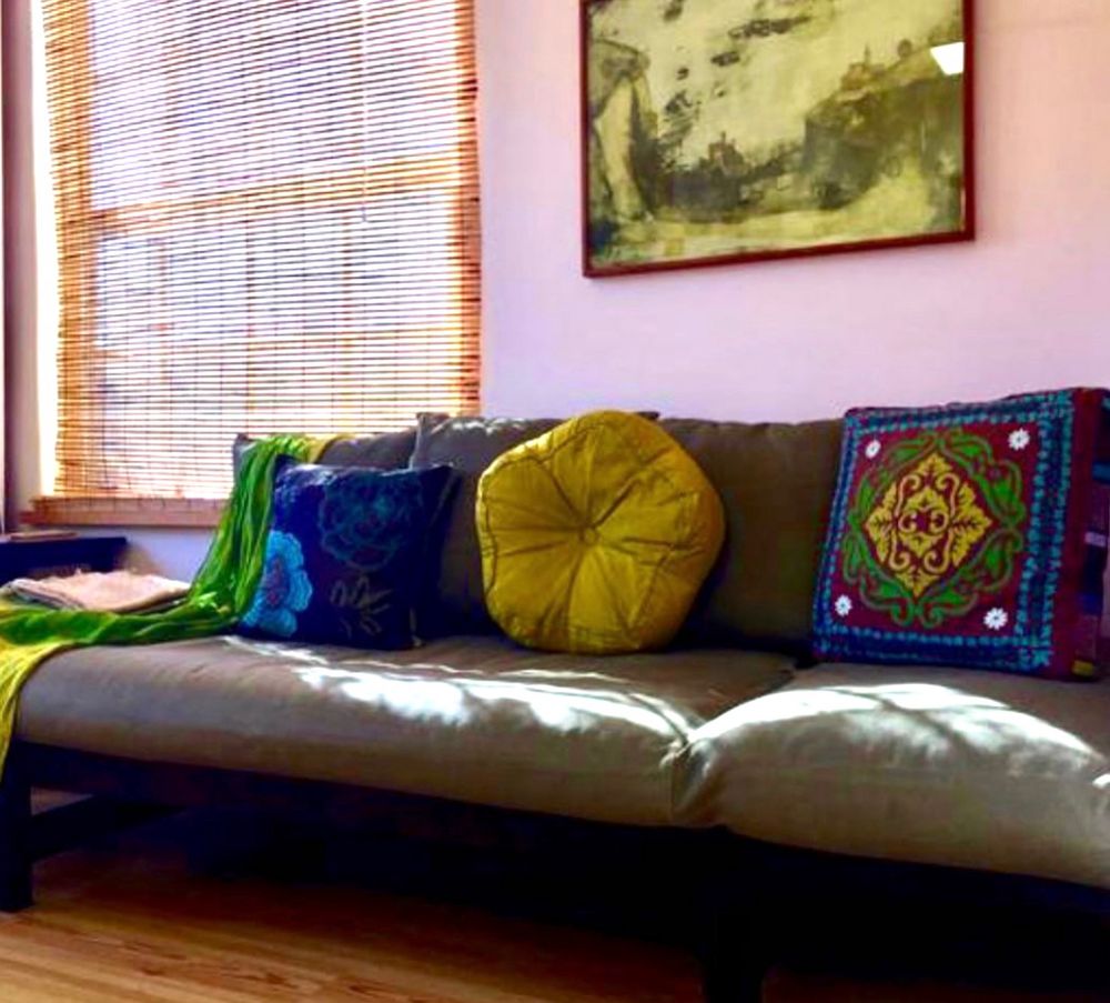 Sofa with silk chartreuse and turquoise cushions and green and gold meditation shawls in serene, sunny setting. Soothing green artwork. 
