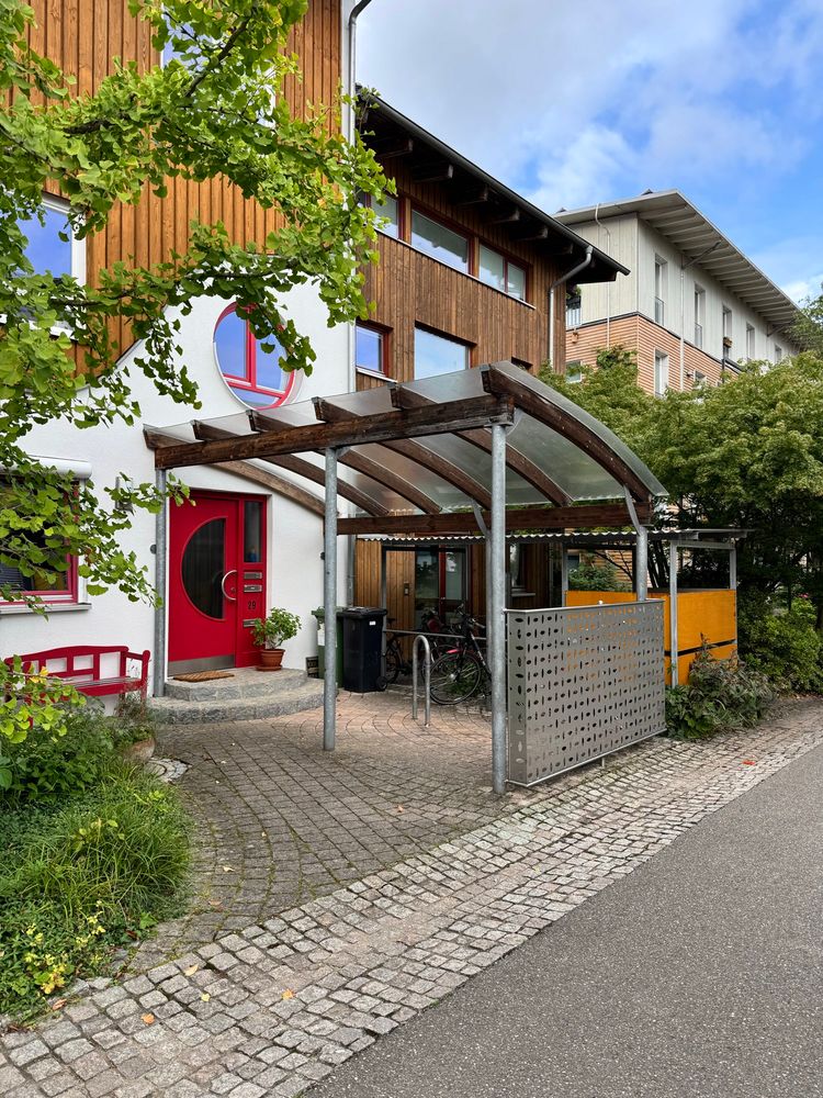 A street scene from Vauban showing row houses of slightly different heights, with green front gardens and covered bicycle parking facilities 
