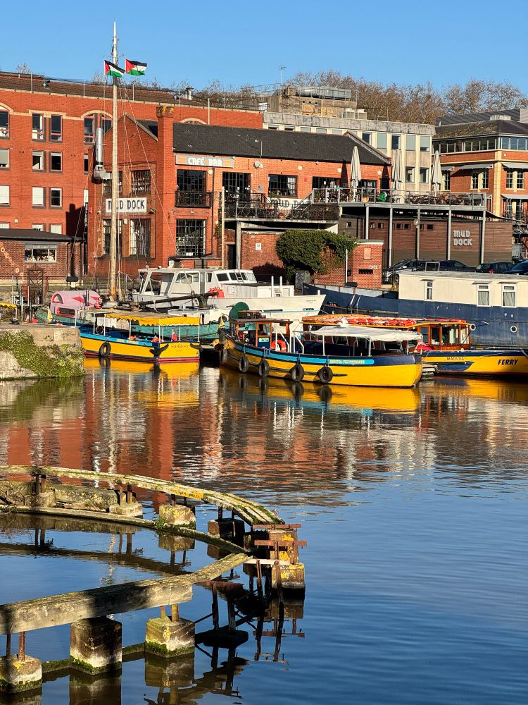 Sunny Bristol harbour with colourful boats and Mud Dock cafe in the background 