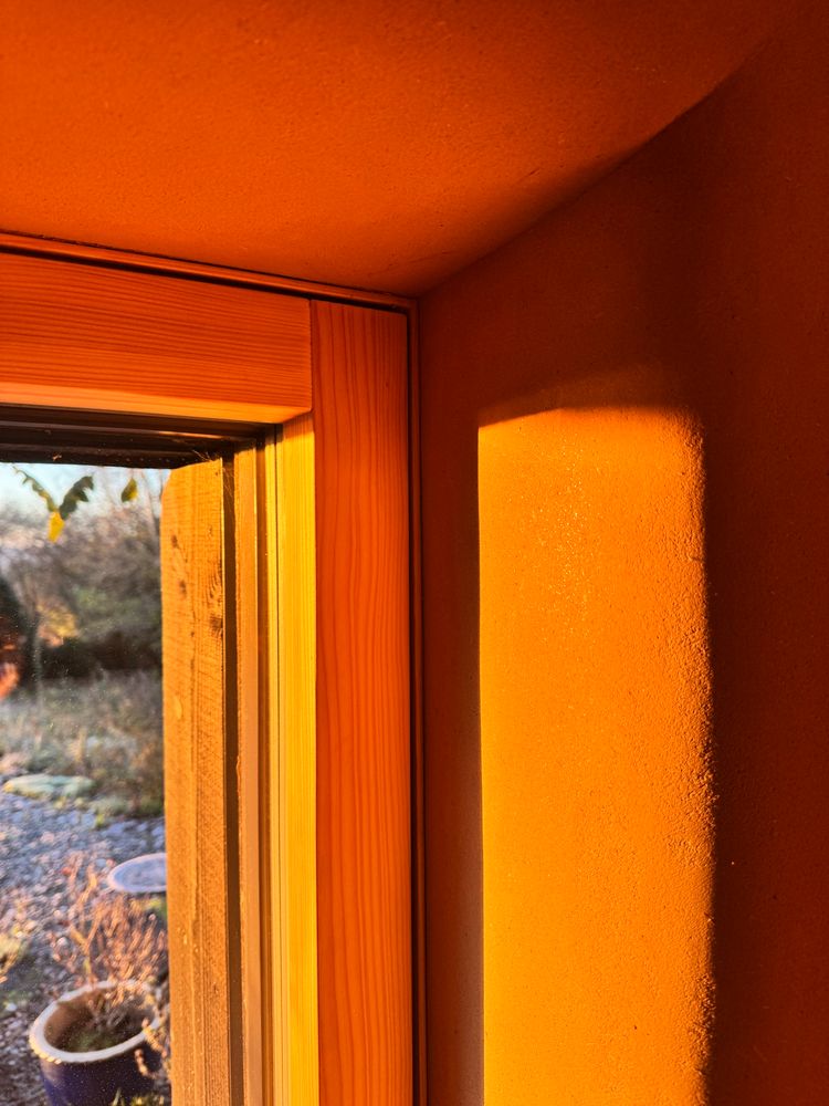 Home interior flooded with warm morning light. Detail of a window with curved clay plastered reveals