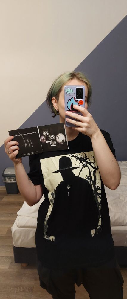 a person with faded green hair in a WITCHZ t-shirt holding signed santi minogo album