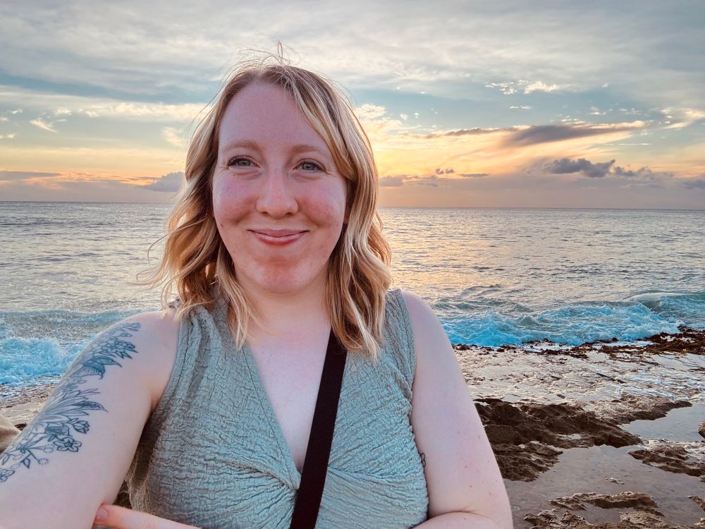 Selfie of myself while in Hawaii. There’s the ocean and a sunset behind me.